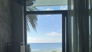Une chambre avec vue sur la plage, une grande fenêtre, un ventilateur de plafond et un banc en bois.