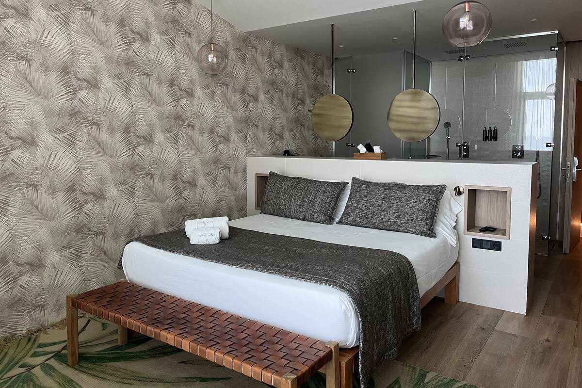 Een moderne slaapkamer met een bed, een bankje en een kaptafel met spiegel.