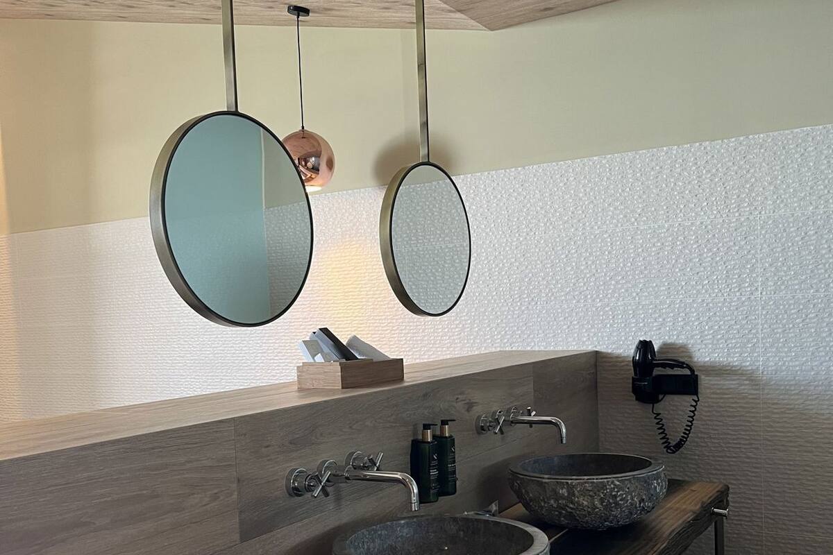 Een badkamer met een houten wastafelmeubel, twee ronde spiegels, een stenen wastafel en een telefoon.
