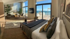 Een ruime slaapkamer met een groot bed, uitzicht op het strand en een balkon met een stoel.
