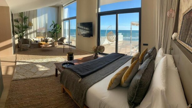 Une chambre spacieuse avec un grand lit, une vue sur la plage et un balcon équipé d’une chaise.