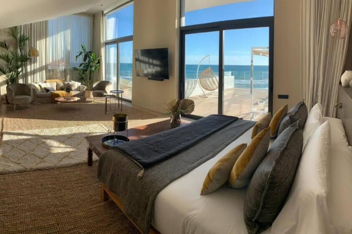 Een ruime slaapkamer met een groot bed, uitzicht op het strand en een balkon met een stoel.