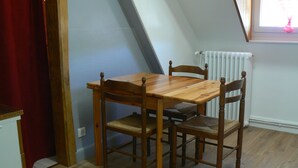 A dining area with a wooden table and chairs, a radiator, and a window with curtains. - Villa des Familles - Antarès - Peace and quiet at La Bourboule (La Bourboule)