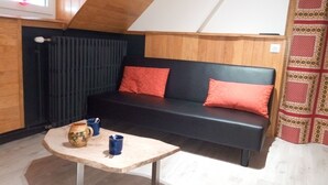 A cozy room with a black sofa, two red cushions, a small table with a ceramic jug and a blue mug, and a radiator. - Villa des Familles - Antarès - Peace and quiet at La Bourboule (La Bourboule)
