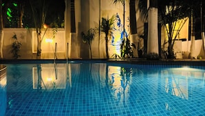 A swimming pool with clear blue tiles, surrounded by tropical plants and a building with a mural. - JP Resort (Arambol)