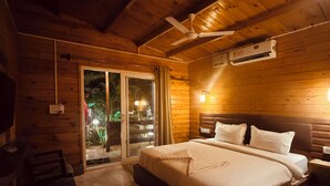 A wooden cabin bedroom with a bed, a ceiling fan, an air conditioning unit, and a sliding glass door leading to an outdoor area. - JP Resort (Arambol)