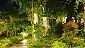 A nighttime garden pathway with palm trees and illuminated plants, leading to a building with a tiled entrance. - JP Resort (Arambol)
