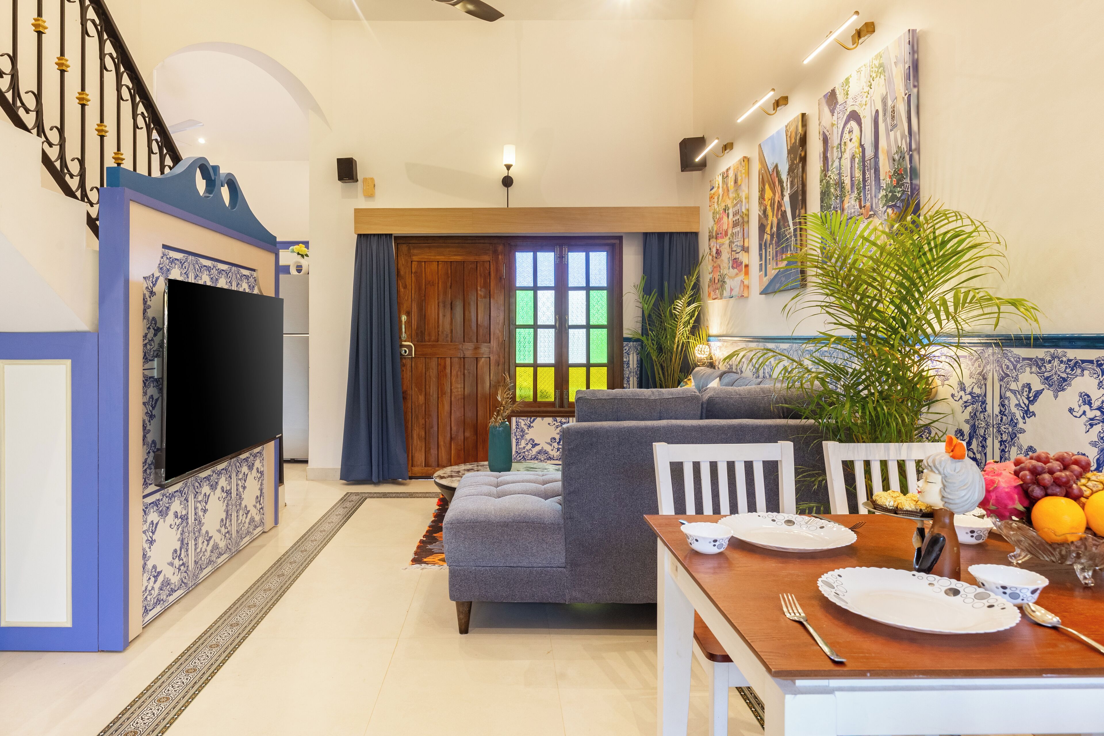 A living room with a TV, sofa, dining table, chairs, and a staircase.