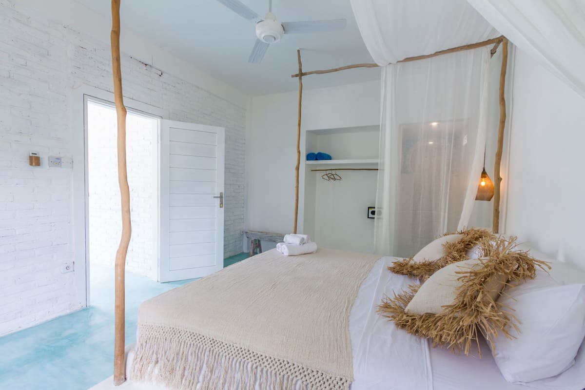 A bedroom with a bed, a ceiling fan, a white door, and a window.