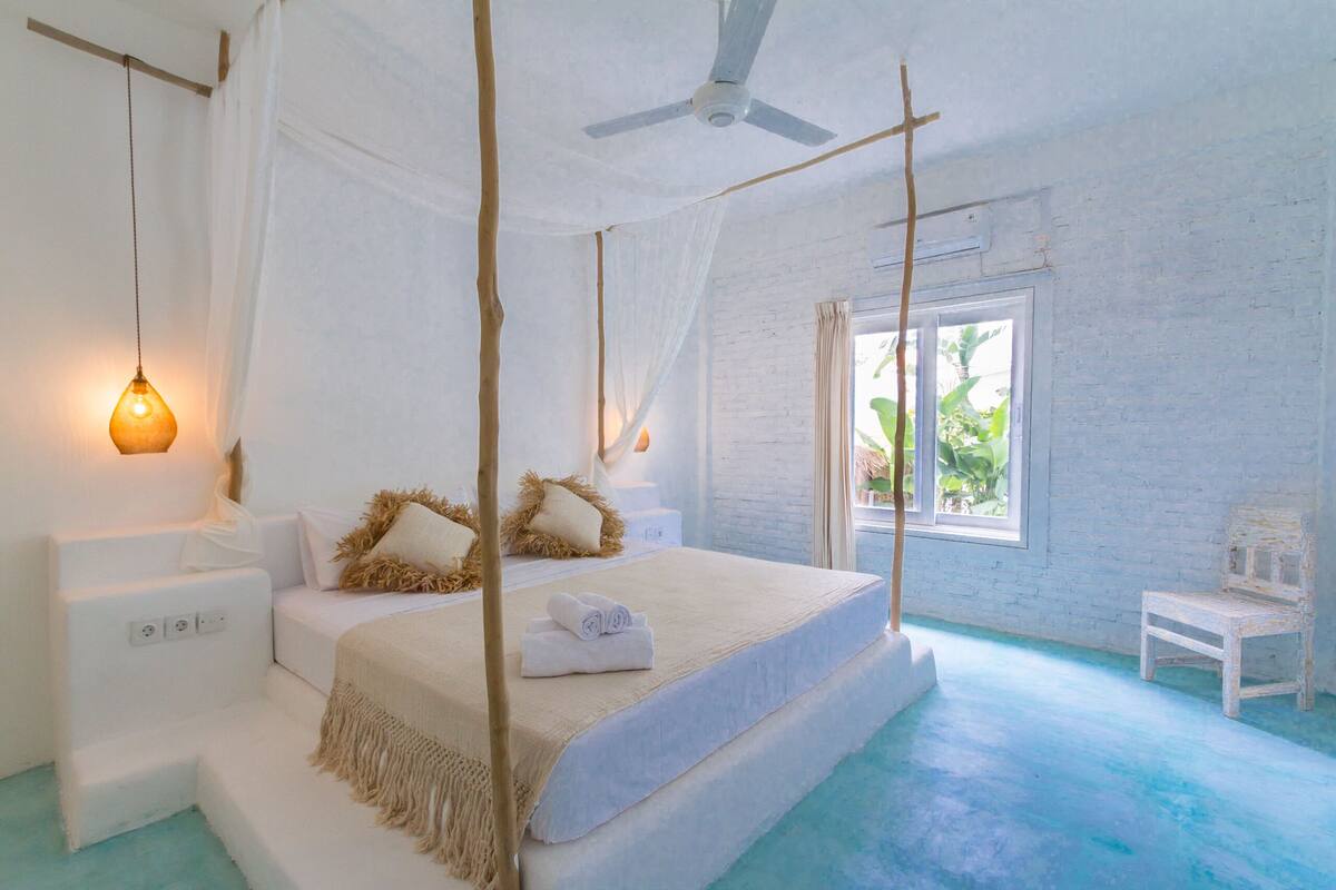 A bedroom with a bed, bedside tables, a ceiling fan, and a window with a view of greenery.