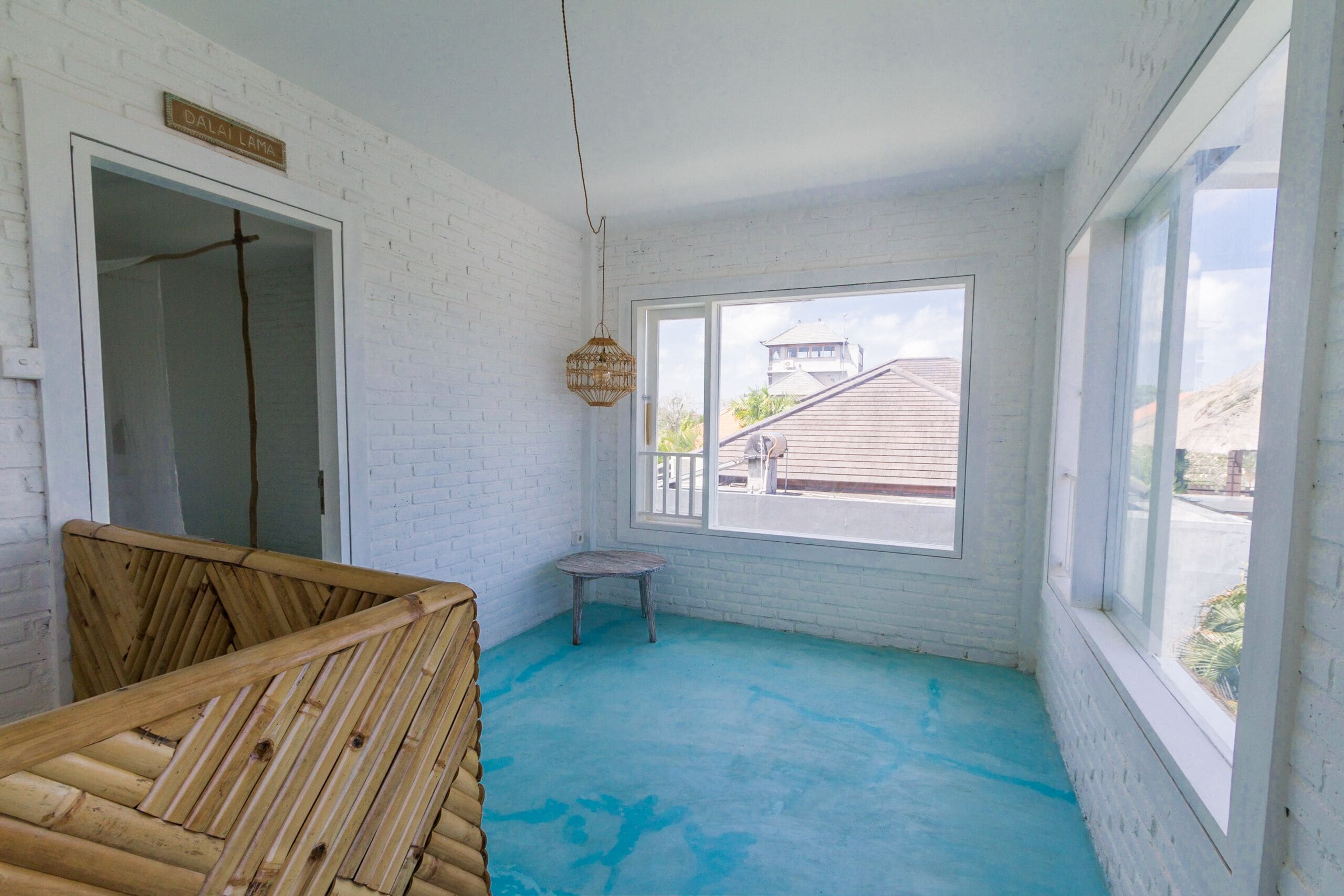A room with a wooden bed, a small stool, a window with a view of a building, and a sign on the wall.