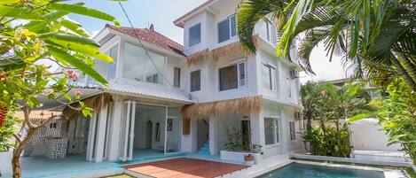 A two-story house with a swimming pool, a covered patio, and a thatched roof.