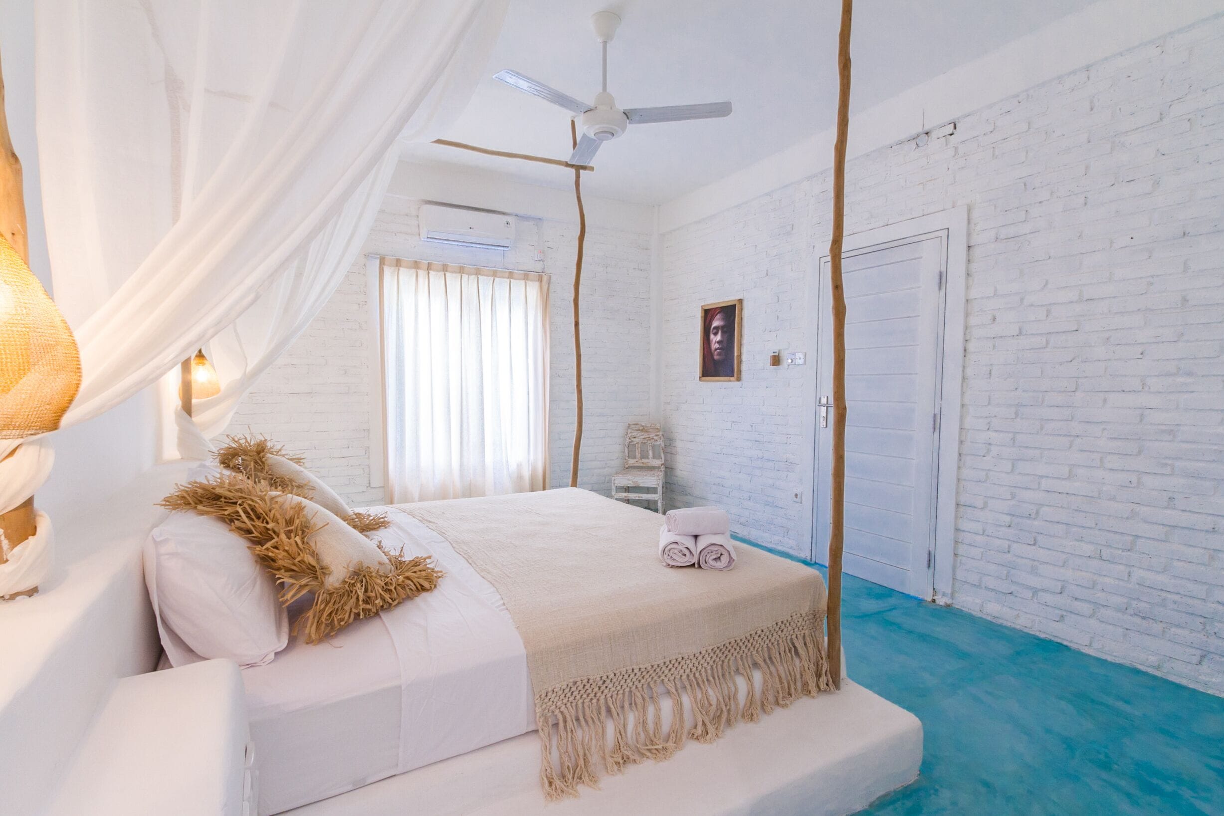 A bedroom with a white bed, a ceiling fan, and a white brick wall.