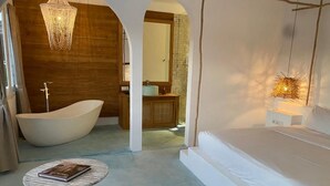 A bedroom with a large bed, a bathtub, and a small table with a book. - Guru Canggu (Canggu)