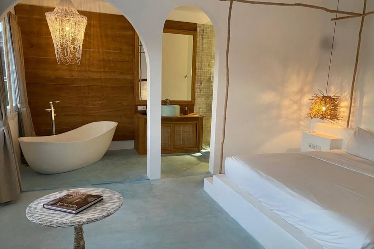 A bedroom with a large bed, a bathtub, and a small table with a book.