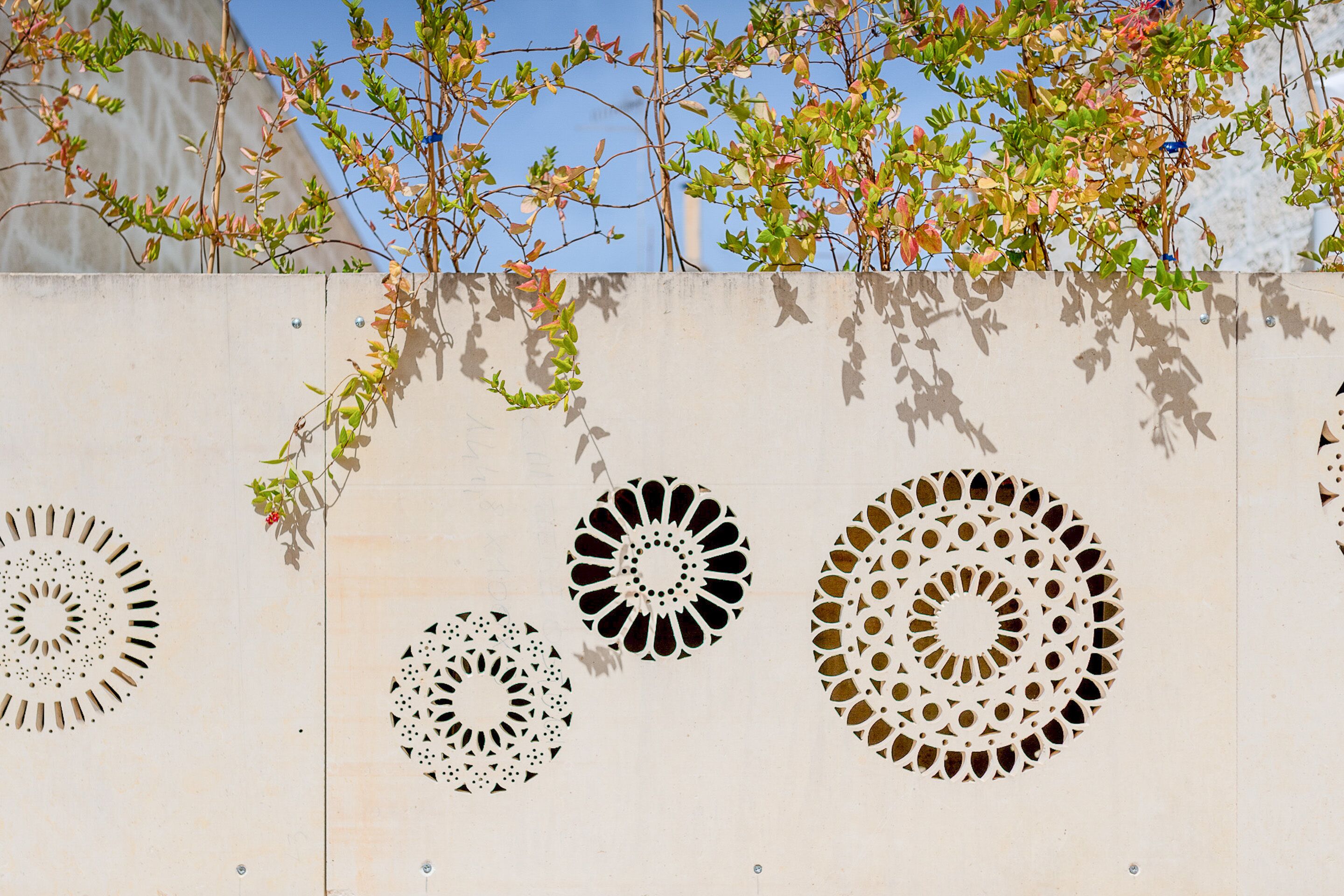 Un mur orné de motifs géométriques découpés et une branche d’arbre avec des feuilles vertes.