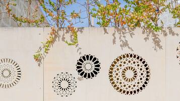 Un mur orné de motifs géométriques découpés et une branche d’arbre avec des feuilles vertes.