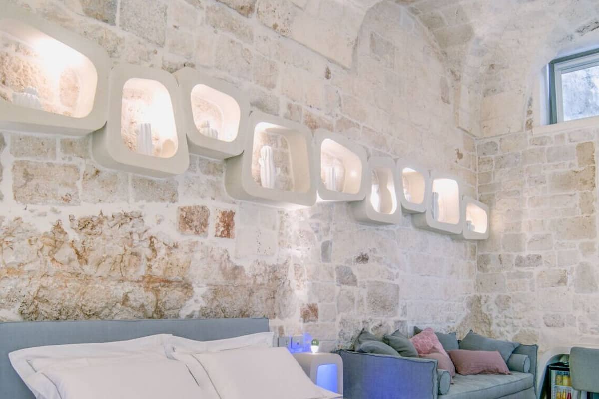A stone-walled room with a bed, a sofa, and a window.