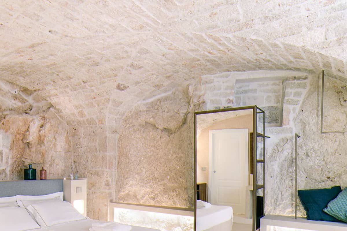 A bedroom with a stone ceiling, a bed with white linens, a bedside table, and a mirror.