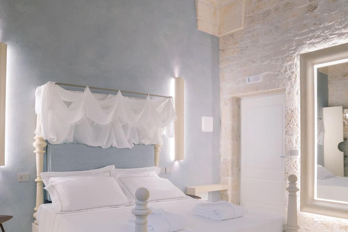 A bedroom with a bed, a bedside table, a mirror, and a stone wall.