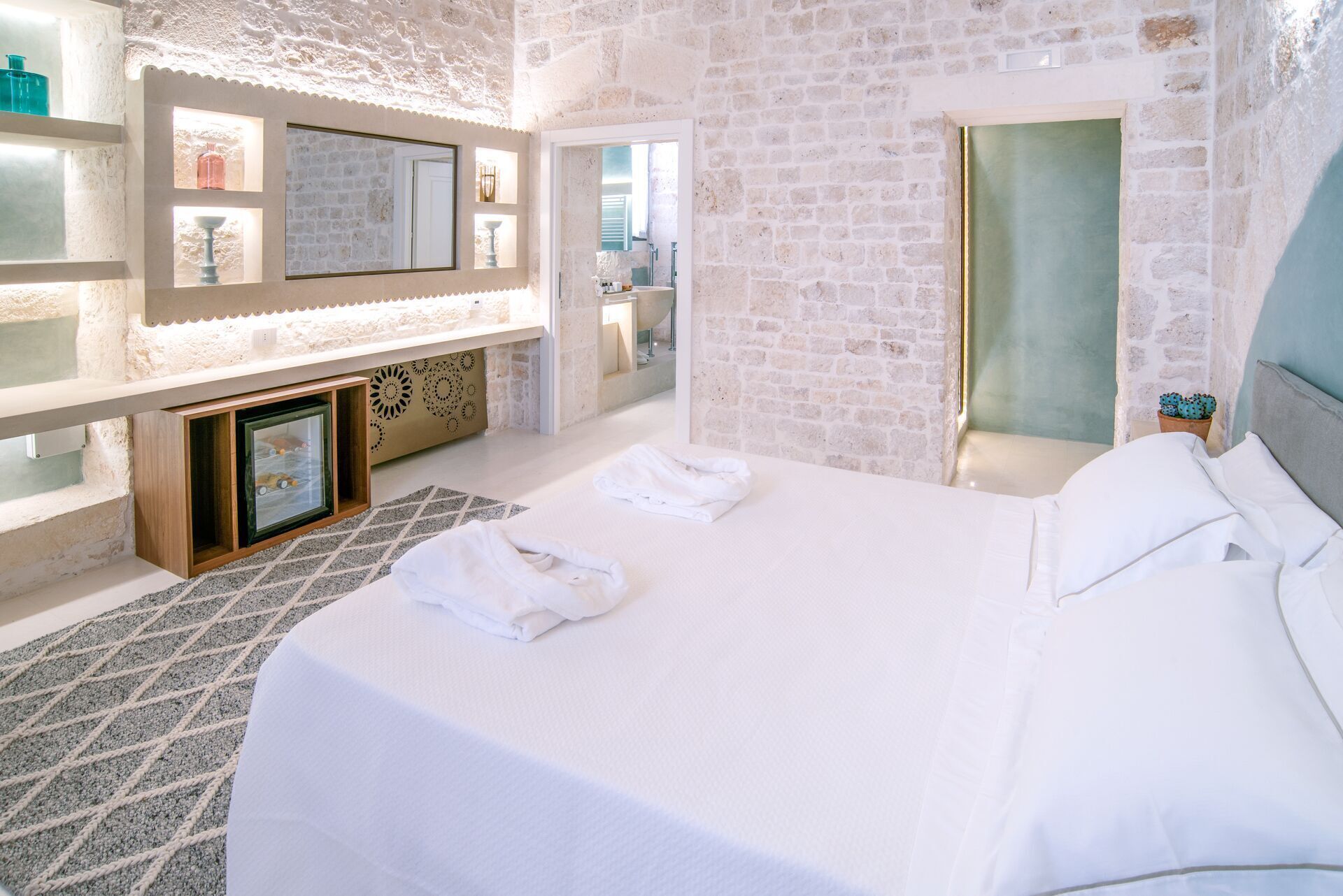 Ein Hotelzimmer mit einem großen Bett, einem integrierten Fernseher, einer kleinen Sitzecke mit Tisch und einem sichtbaren Badezimmer durch eine geöffnete Tür.