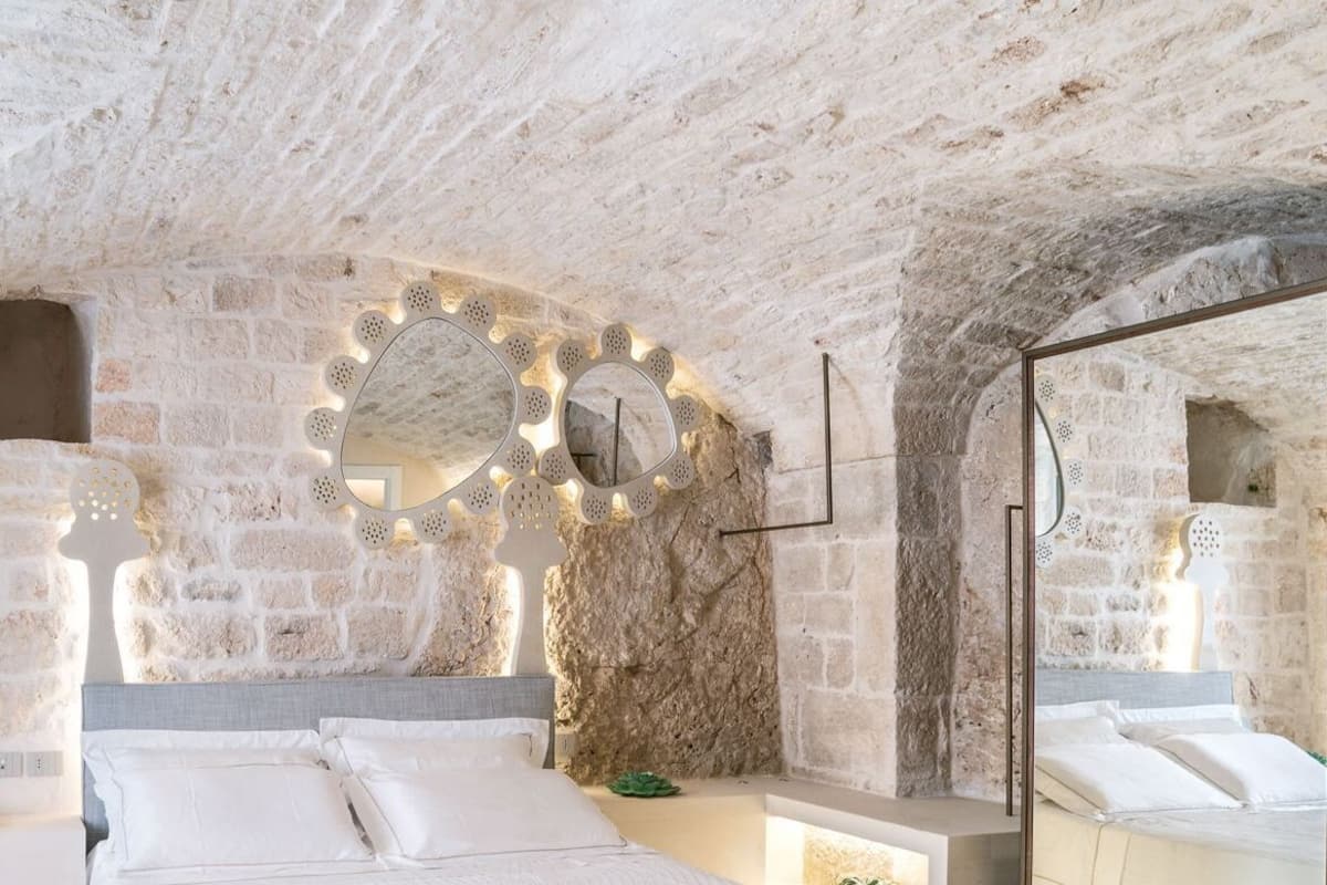 A stone-walled room with two beds, a mirror, and a small table.