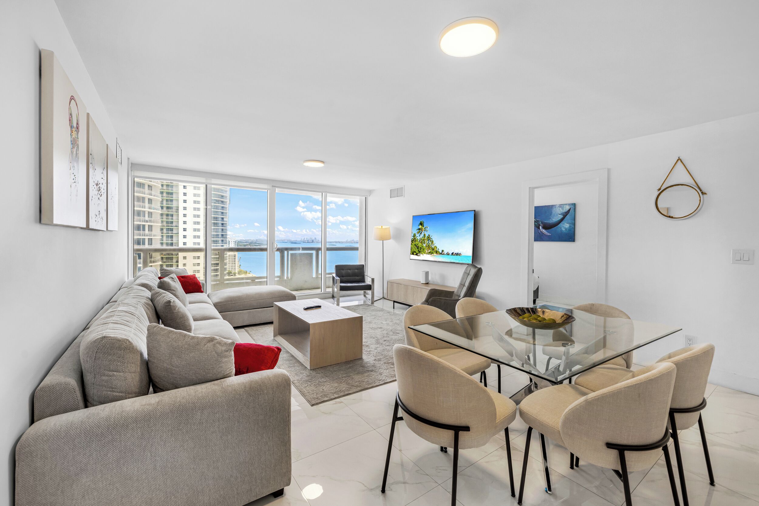 A modern living room with a sofa, coffee table, dining table, chairs, a TV, and artwork on the walls.