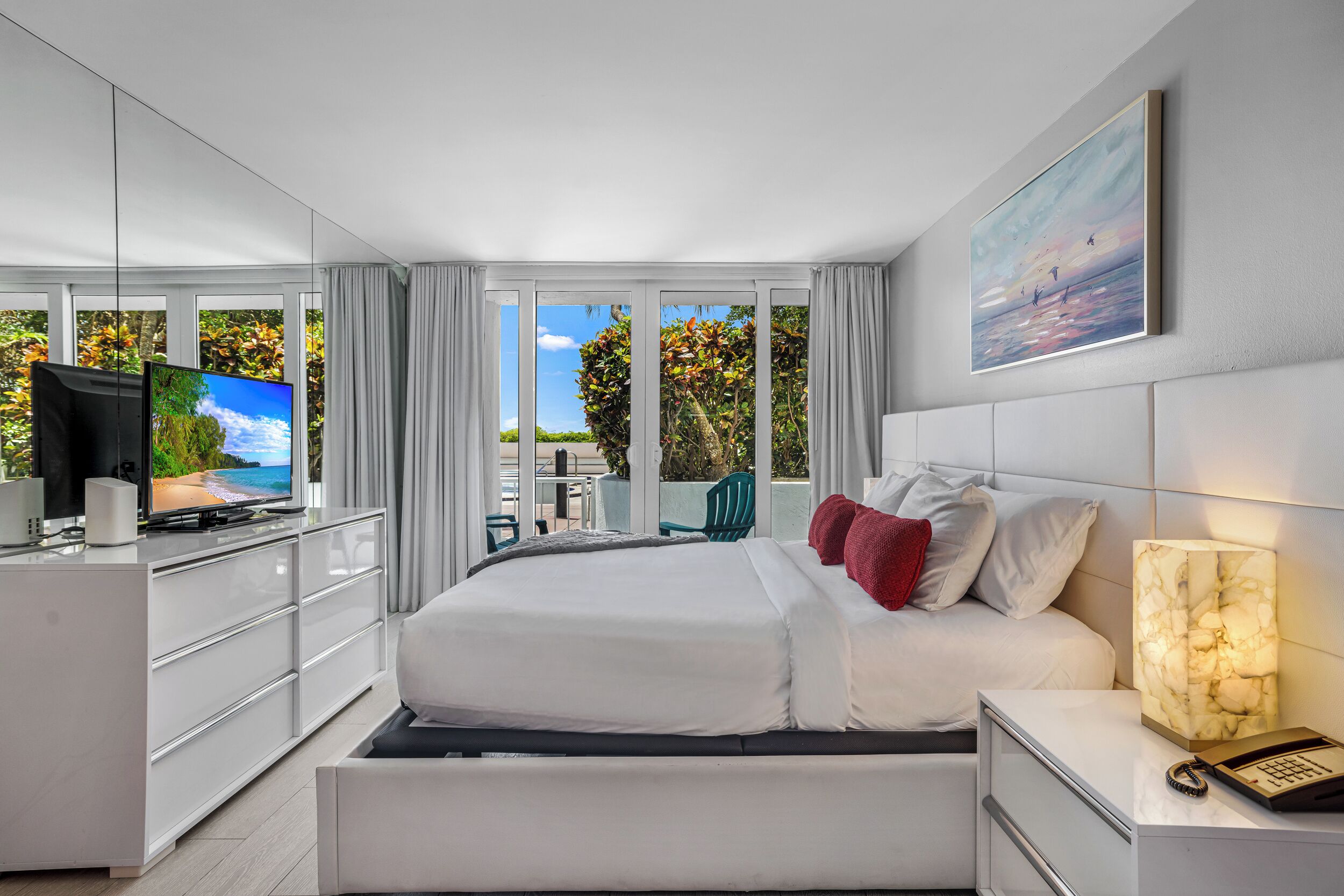 Ein modernes Hotelzimmer mit Bett, Fernseher, Schreibtisch und Blick ins Freie.