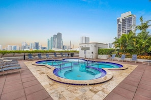 A rooftop pool with a city skyline in the background, surrounded by lounge chairs and a modern building. - Chic Bayfront Condo With Stunning View (Miami)
