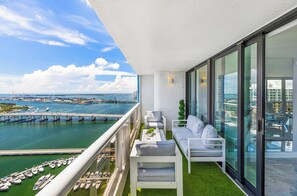 Varanda com vista para um porto de iates e uma ponte, mobiliada com sofás brancos e uma mesa pequena.