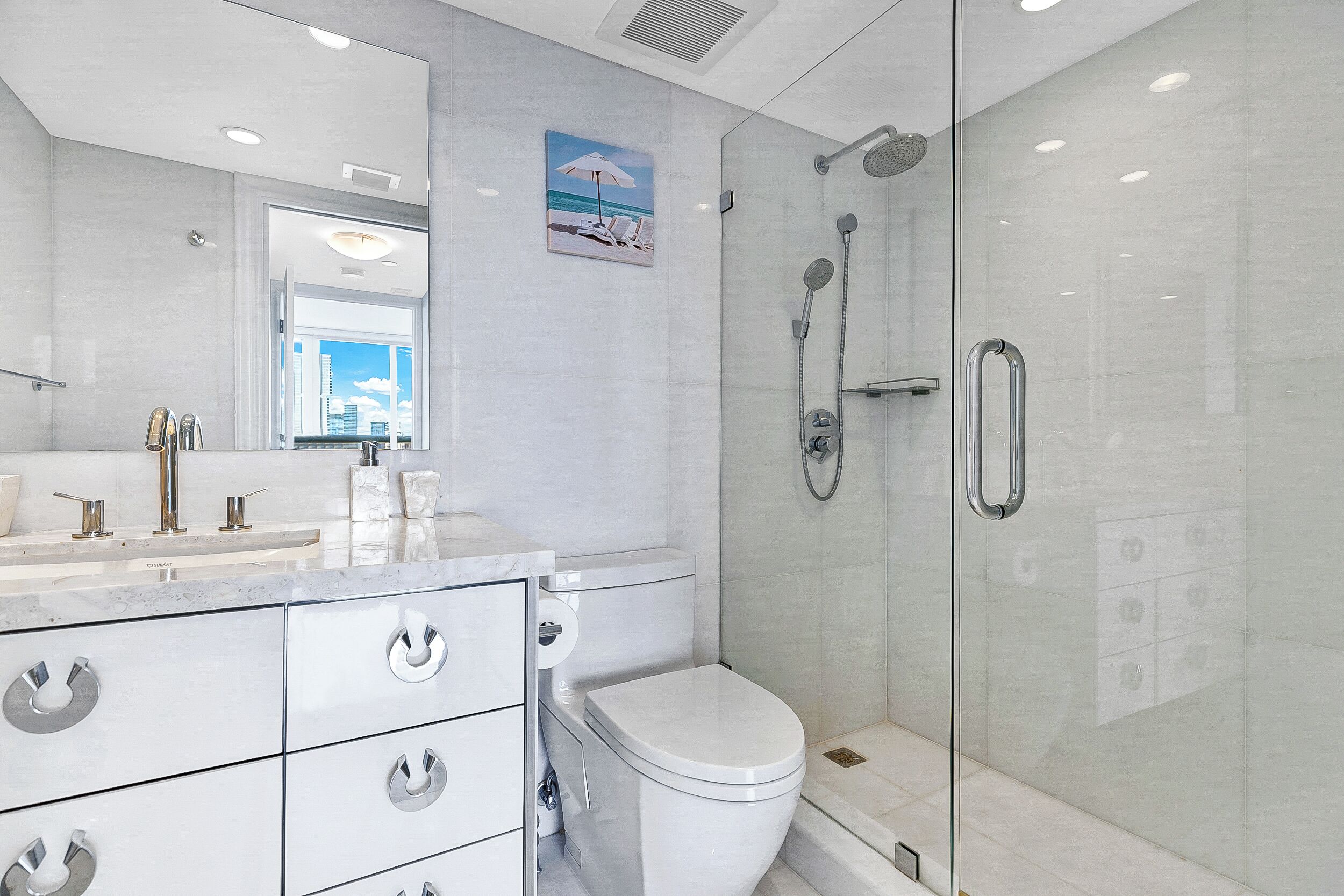 Een moderne badkamer met een douchecabine van glas, een wit toilet en een marmeren wastafel met zilveren handgrepen.