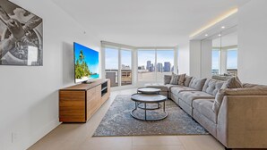 A modern living room with a large window, a sofa, a coffee table, and a TV. - Edgewater Bliss With Balcony (Miami)