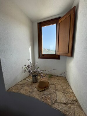 A corner room with a stone floor, a window with wooden shutters, a vase with flowers, and a hat on the floor. - Beautiful mill and views, in the hinterland of the Algarve coast line.<br> (Alcantarilha)