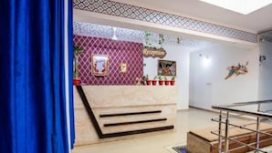 A reception area with a marble counter, a sign that reads "Reception," and a patterned wall. There are potted plants and a staircase visible. - Mgh 114 Hotel Krishna Udaipur (Udaipur)