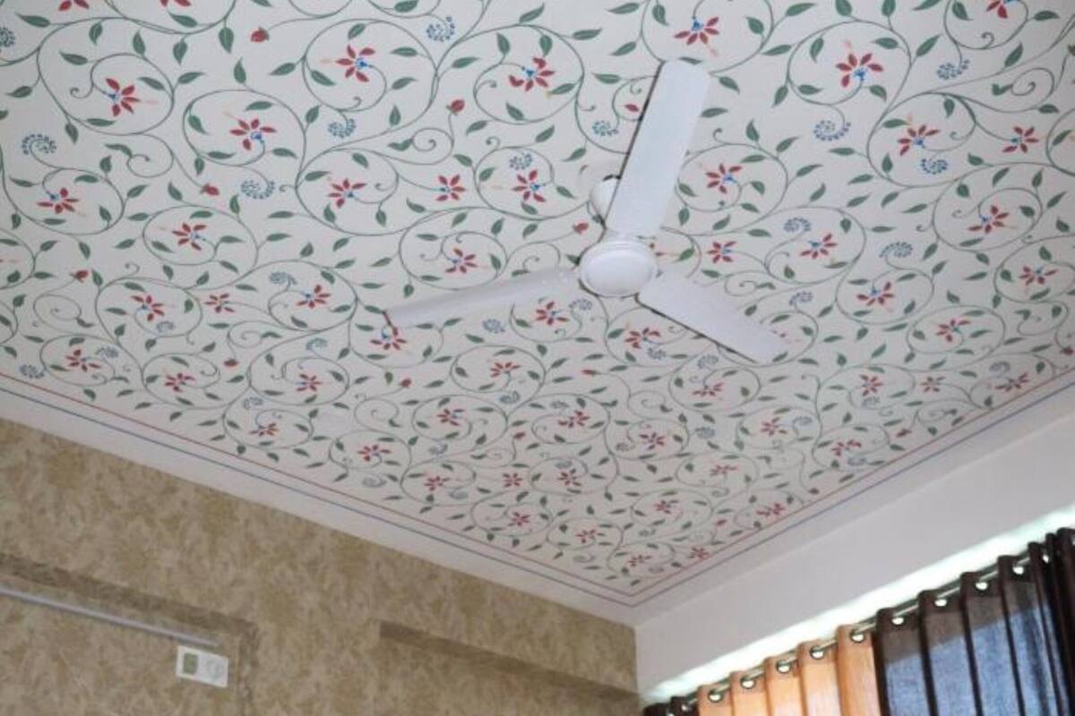 Ein Zimmer mit floralem Deckenmuster, einem Bett mit rotem und weißem Kopfkissen und einem Fenster mit braunen Vorhängen.