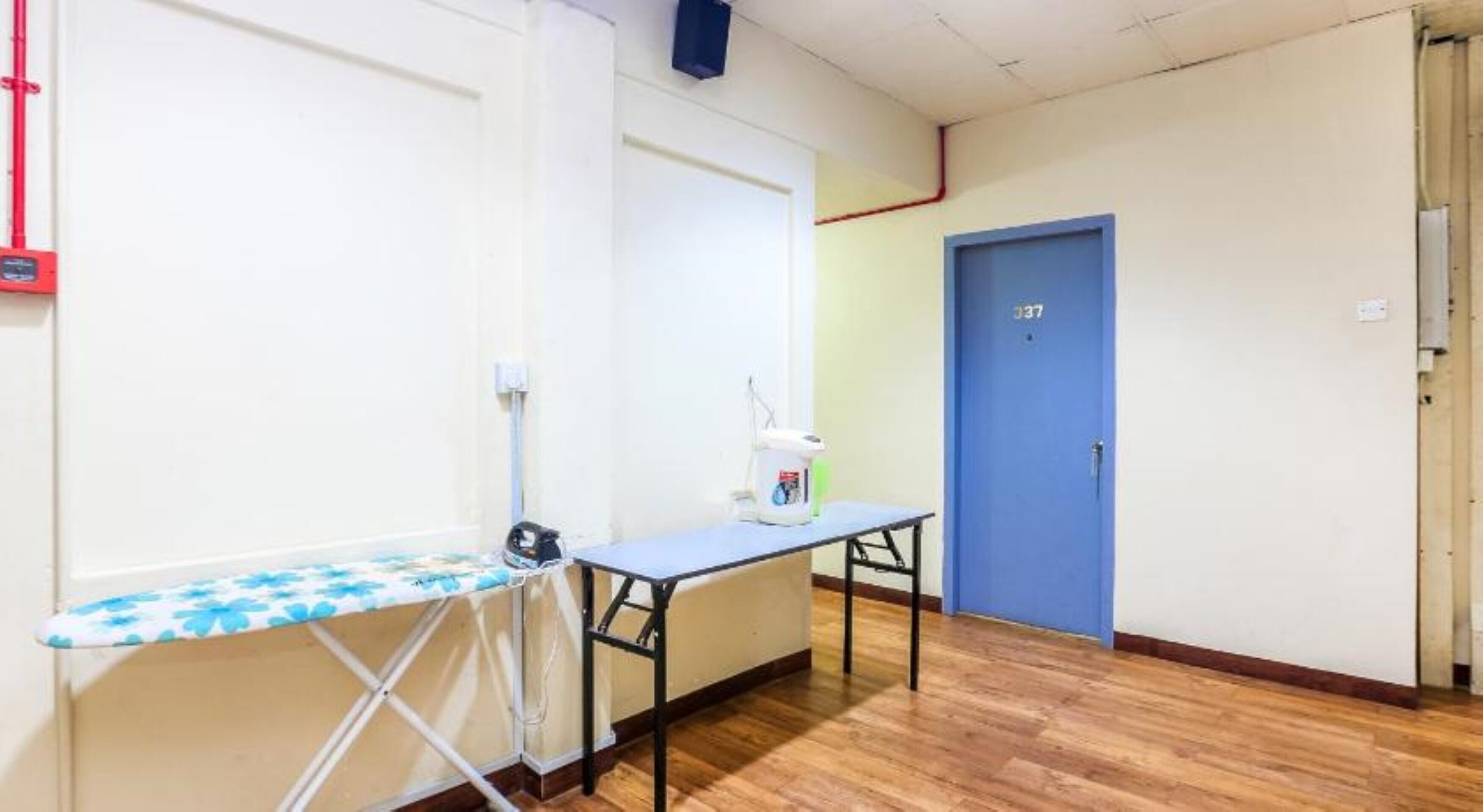 A room with a wooden floor, a blue door, and a table with an ironing board.