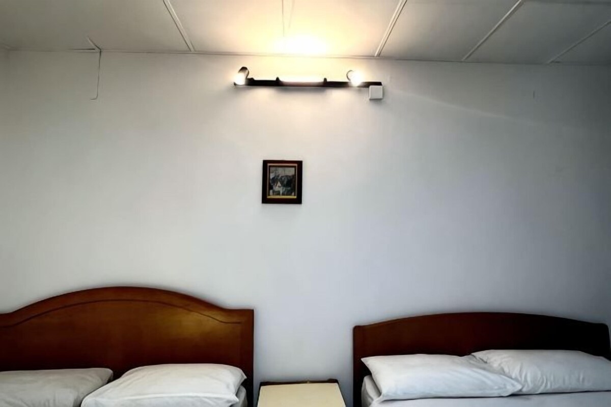 Una habitación con dos camas, una mesita de noche pequeña, una lámpara fijada a la pared y un cuadro enmarcado.