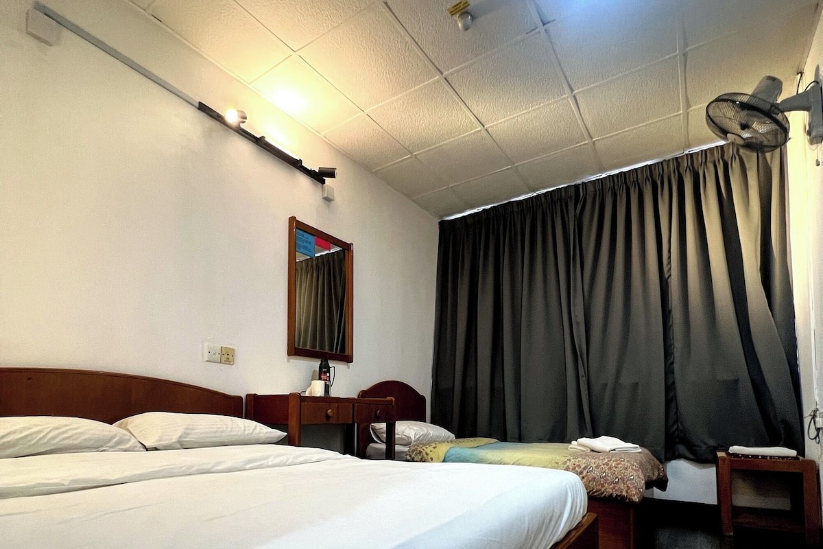 Habitación de hotel con dos camas, un escritorio, una silla, un espejo, un ventilador de techo y una ventana con cortinas.