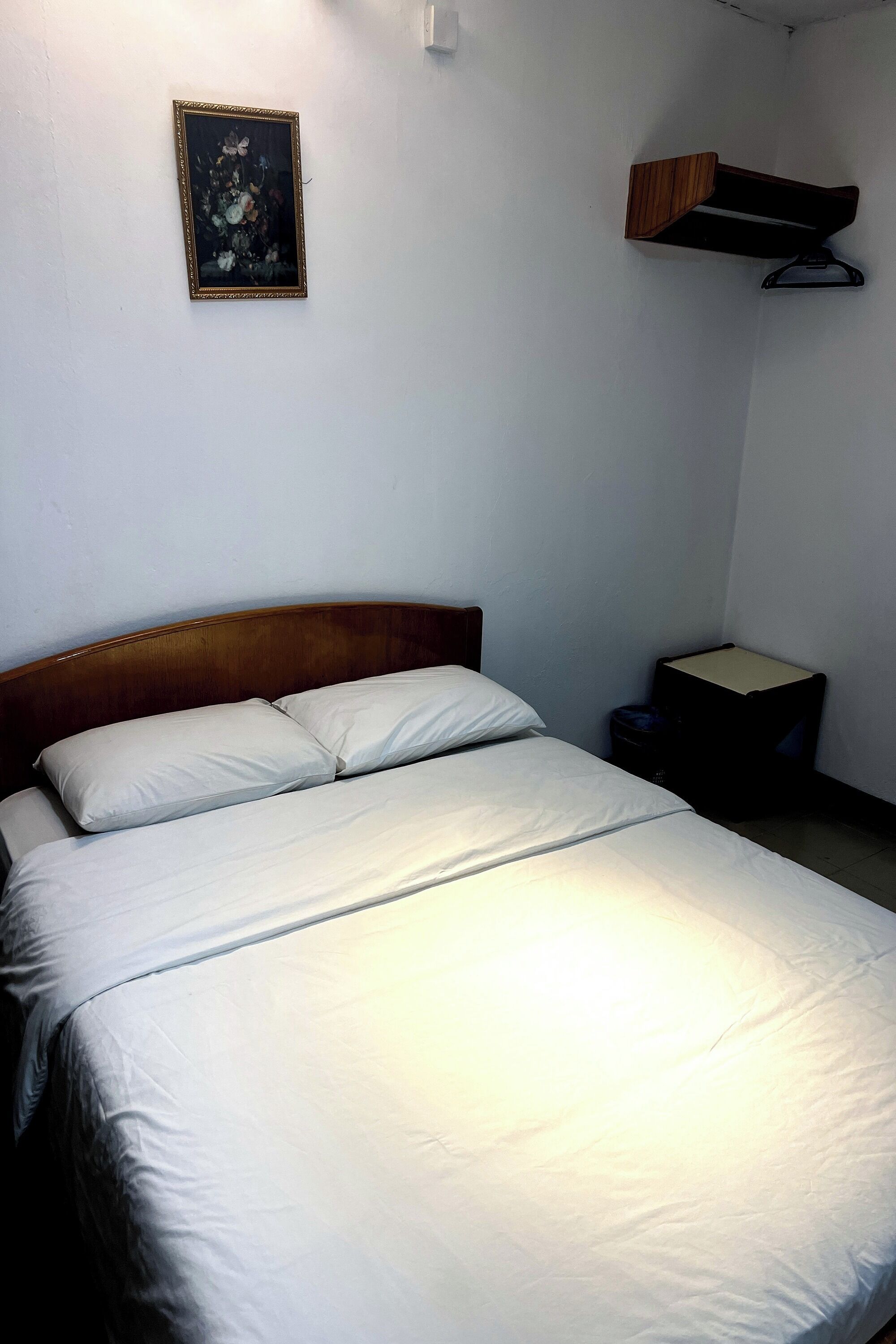 A single bed with white bedding in a room with a wooden headboard. A framed picture hangs on the wall above the bed.