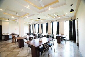 A spacious dining area with multiple tables and chairs, ceiling fans, and large windows with curtains. - Hotel The Royal  (Udaipur)