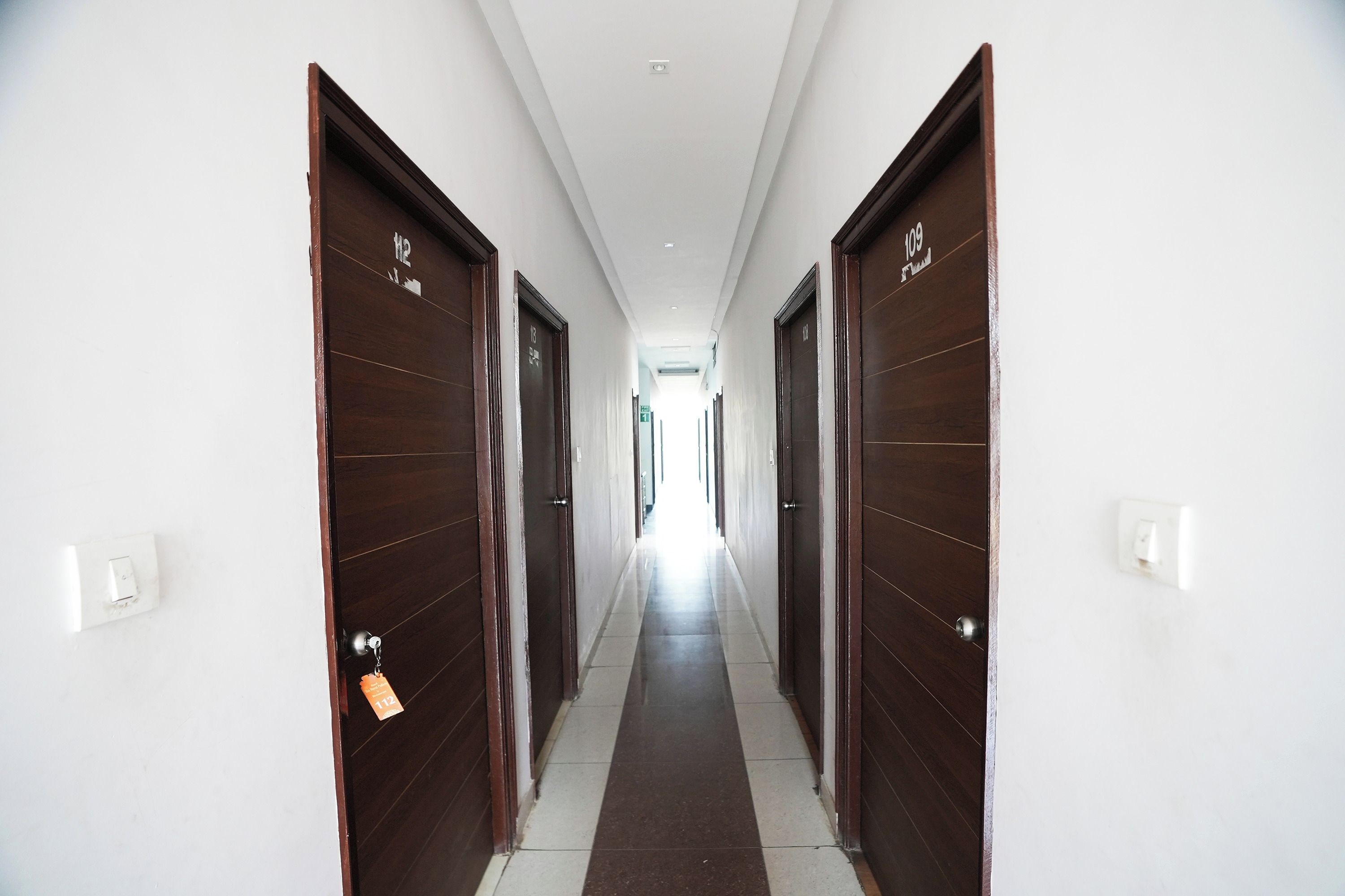 A long, narrow hallway with dark wooden doors on both sides, leading to a bright end.