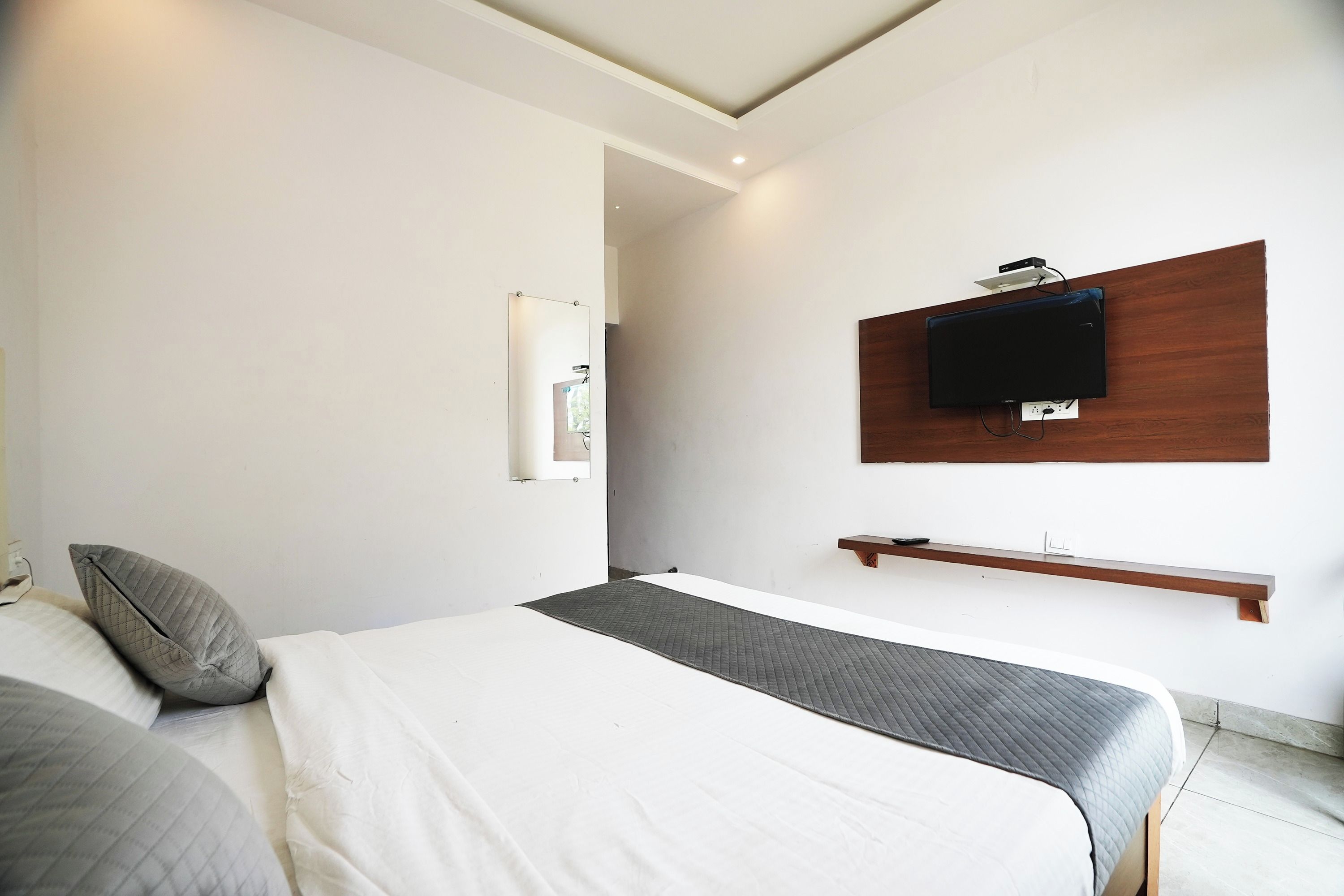 A modern bedroom with a bed, a bedside table, a mounted TV, and a mirror.