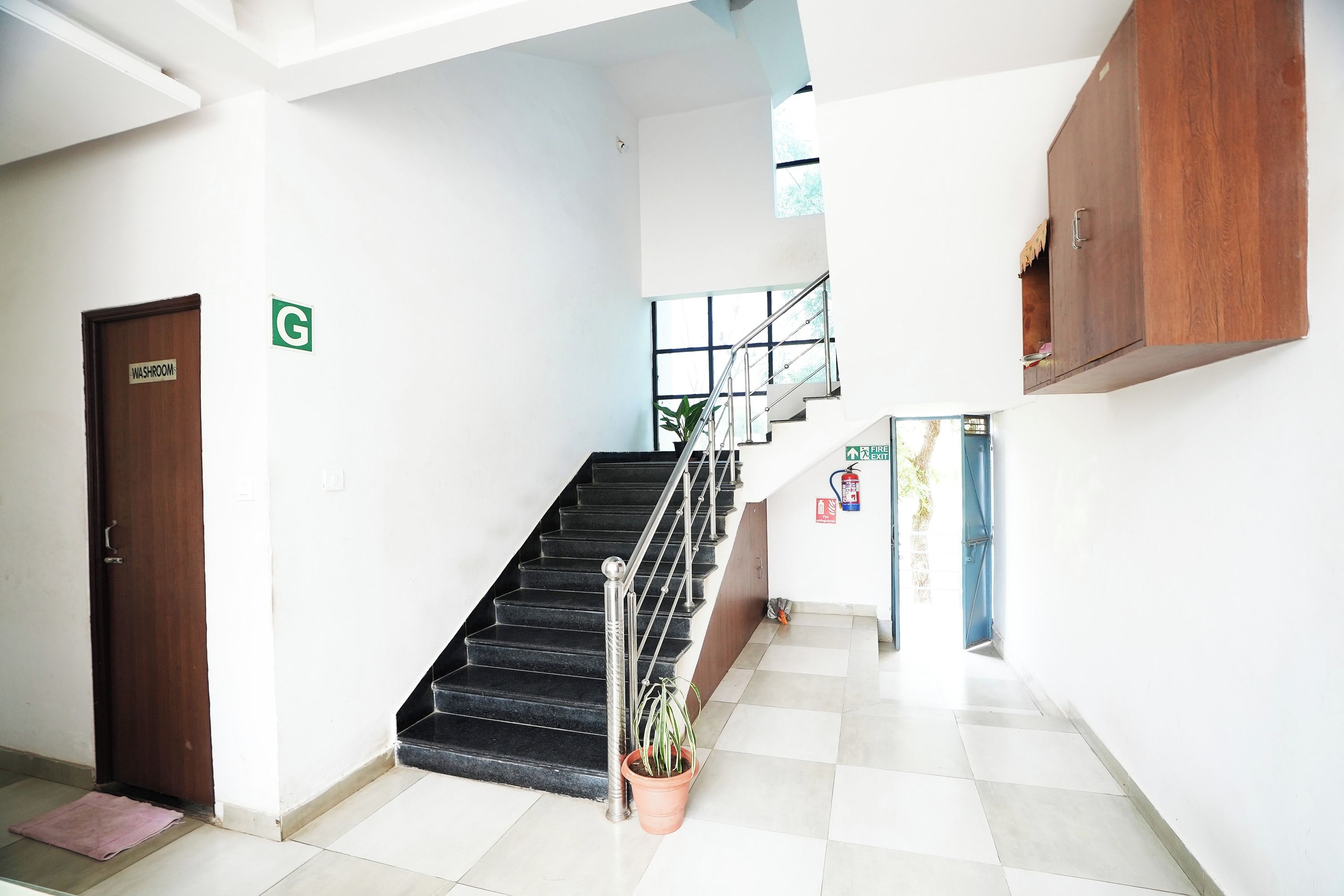 A staircase with a handrail, a fire exit sign, and a washroom sign.