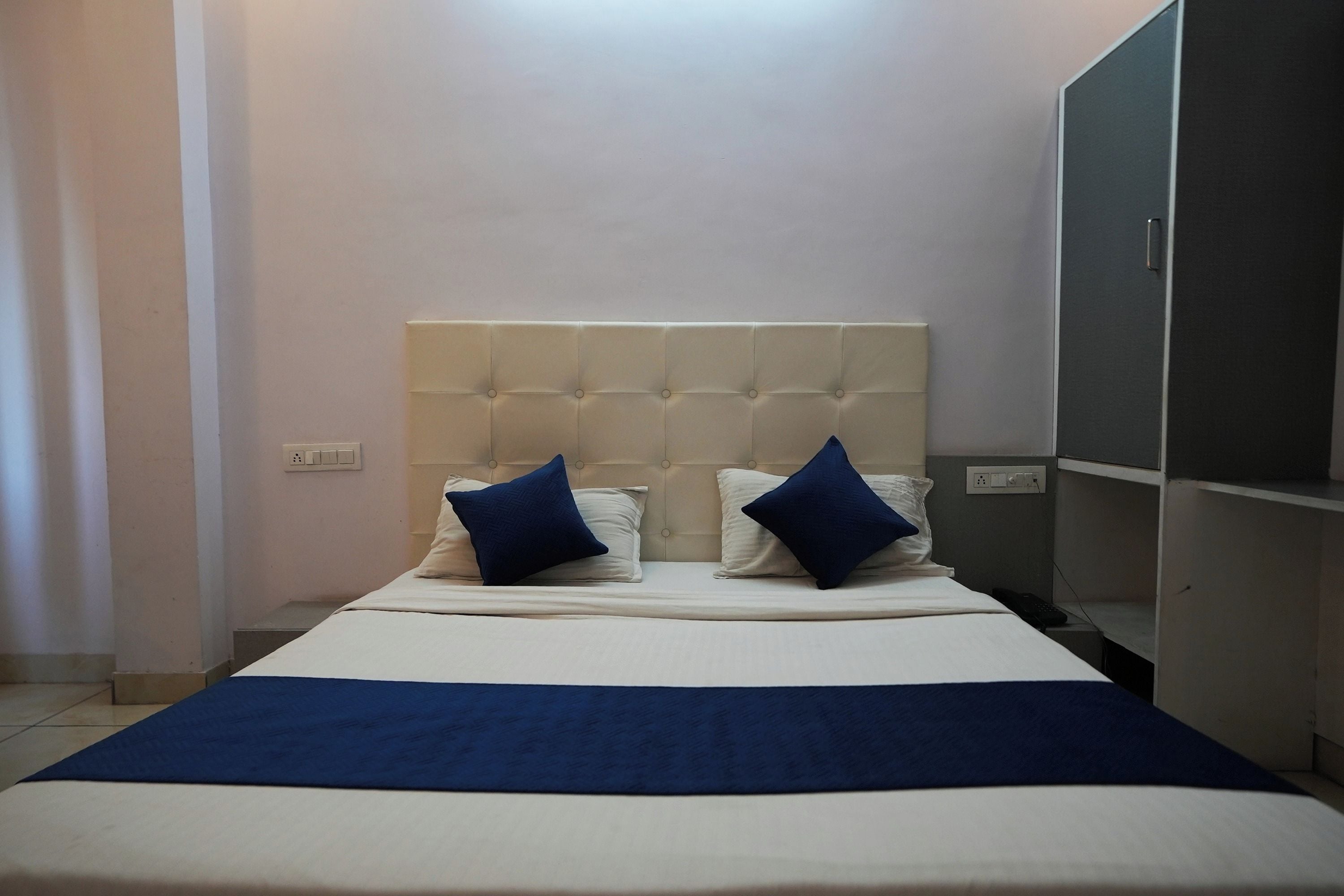 Una habitación de hotel con una cama, dos almohadas, una mesita de noche y un armario.