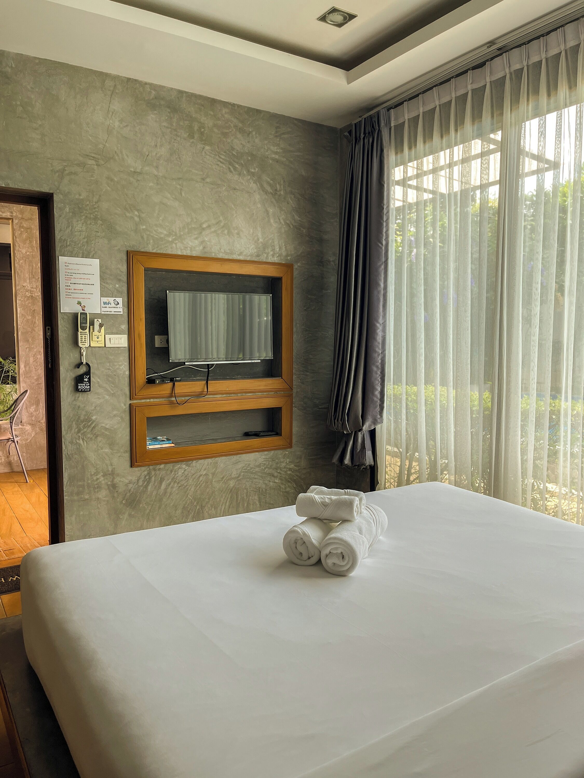 A hotel room with a bed, a mounted TV, a telephone, and a window with curtains.
