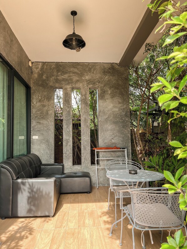Un espacio exterior moderno con un sofá modular, una mesa metálica con sillas y una lámpara colgante.