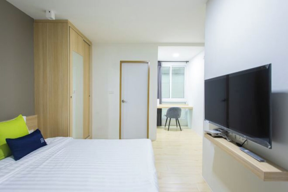 A modern hotel room with a bed, a TV, a desk, and a wardrobe.