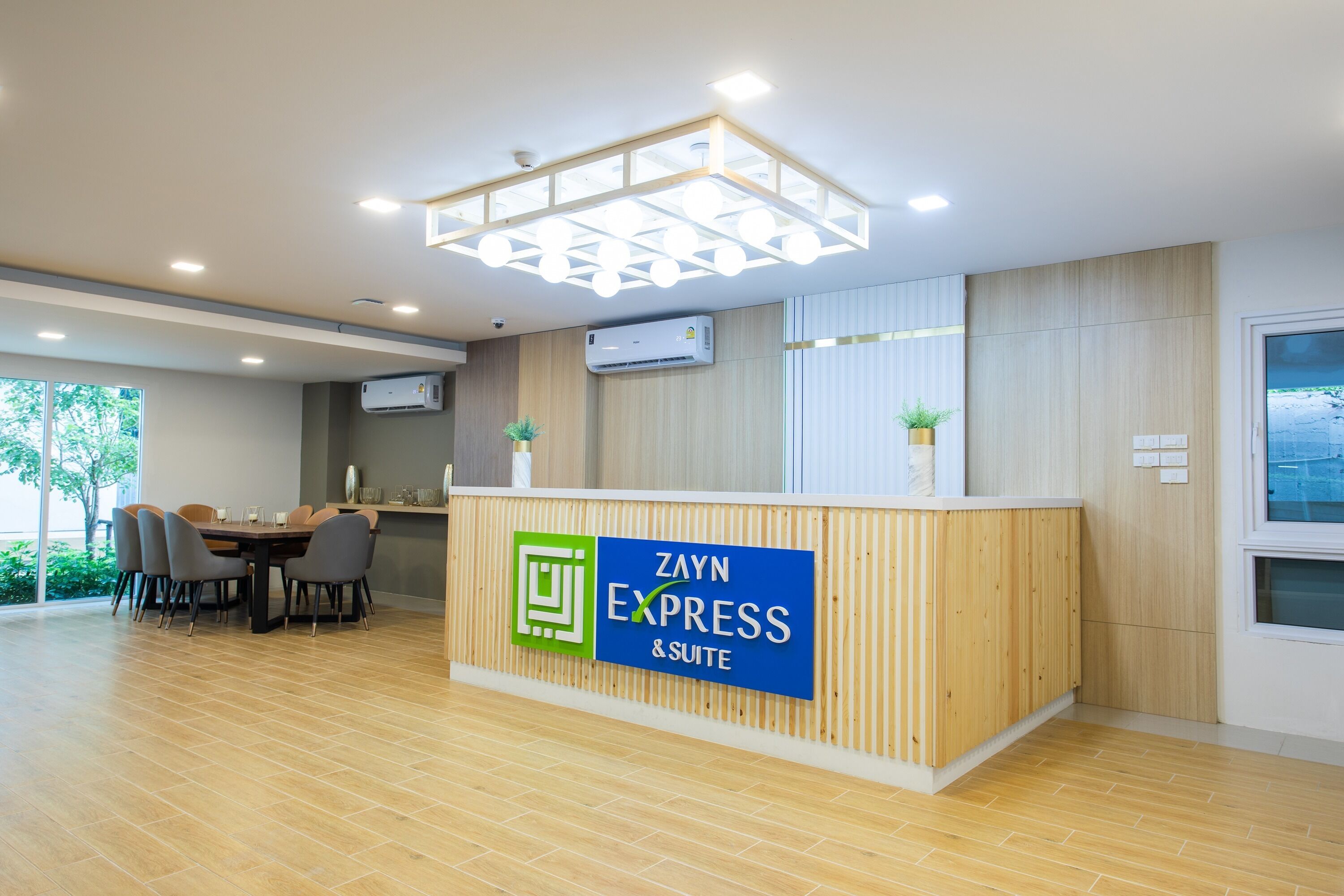Un comptoir d’accueil avec une enseigne indiquant « Zayn Express & Suite », un espace repas avec des chaises et une table, et un plancher en bois.
