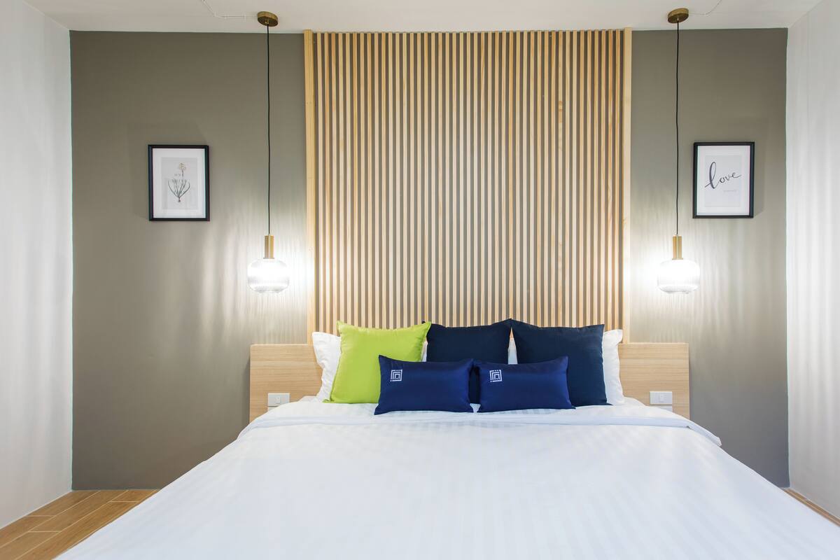 A neatly made bed with white linens, a wooden headboard, and a striped vertical panel behind it.
