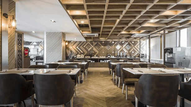 A modern restaurant with a geometric patterned wall, wooden ceiling, and a central counter with a coffee machine. - Zayn Express & Suites (Bangkok)